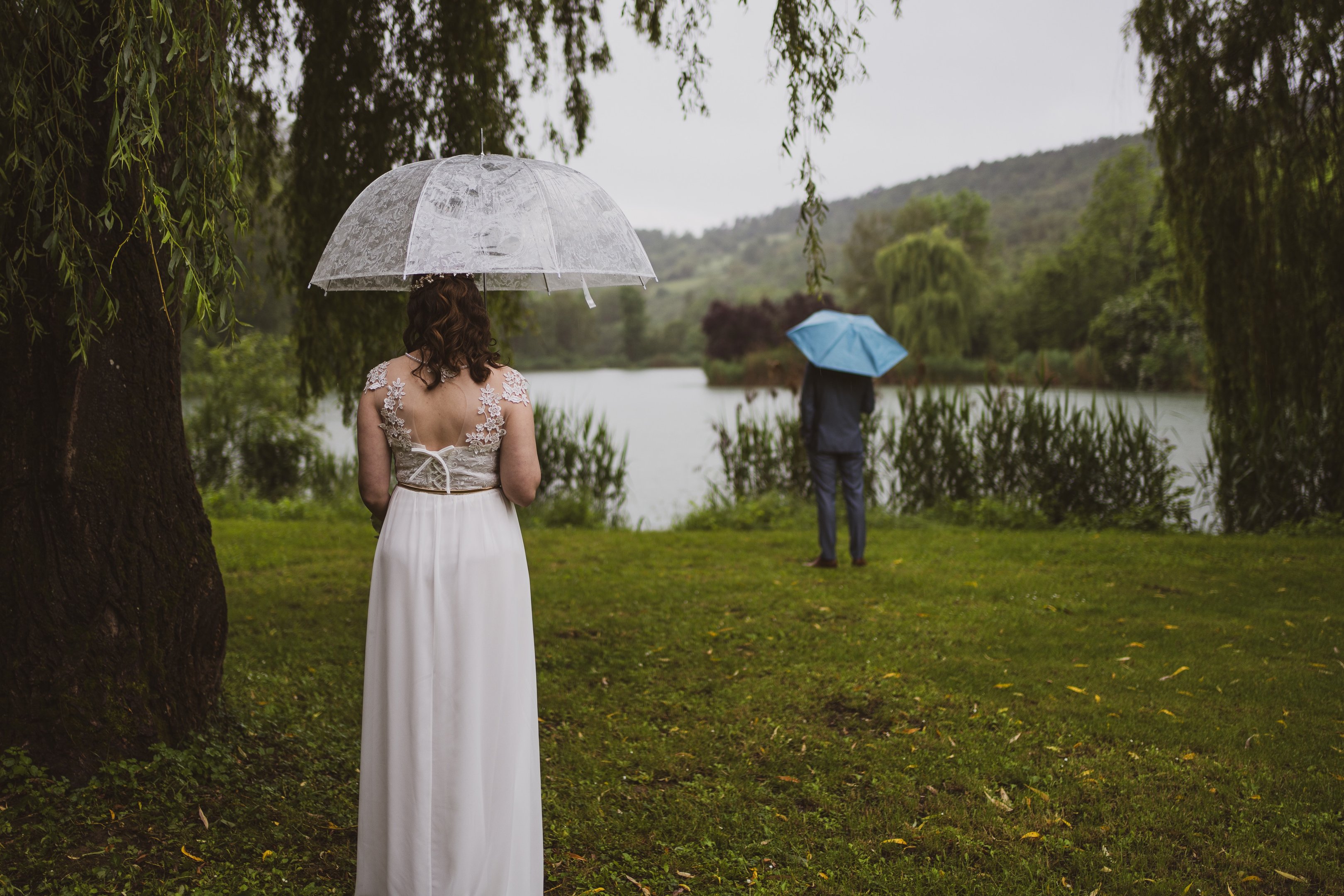 Der First look des Hochzeitspaars am wunderschönen Teich mit Regenschirmen