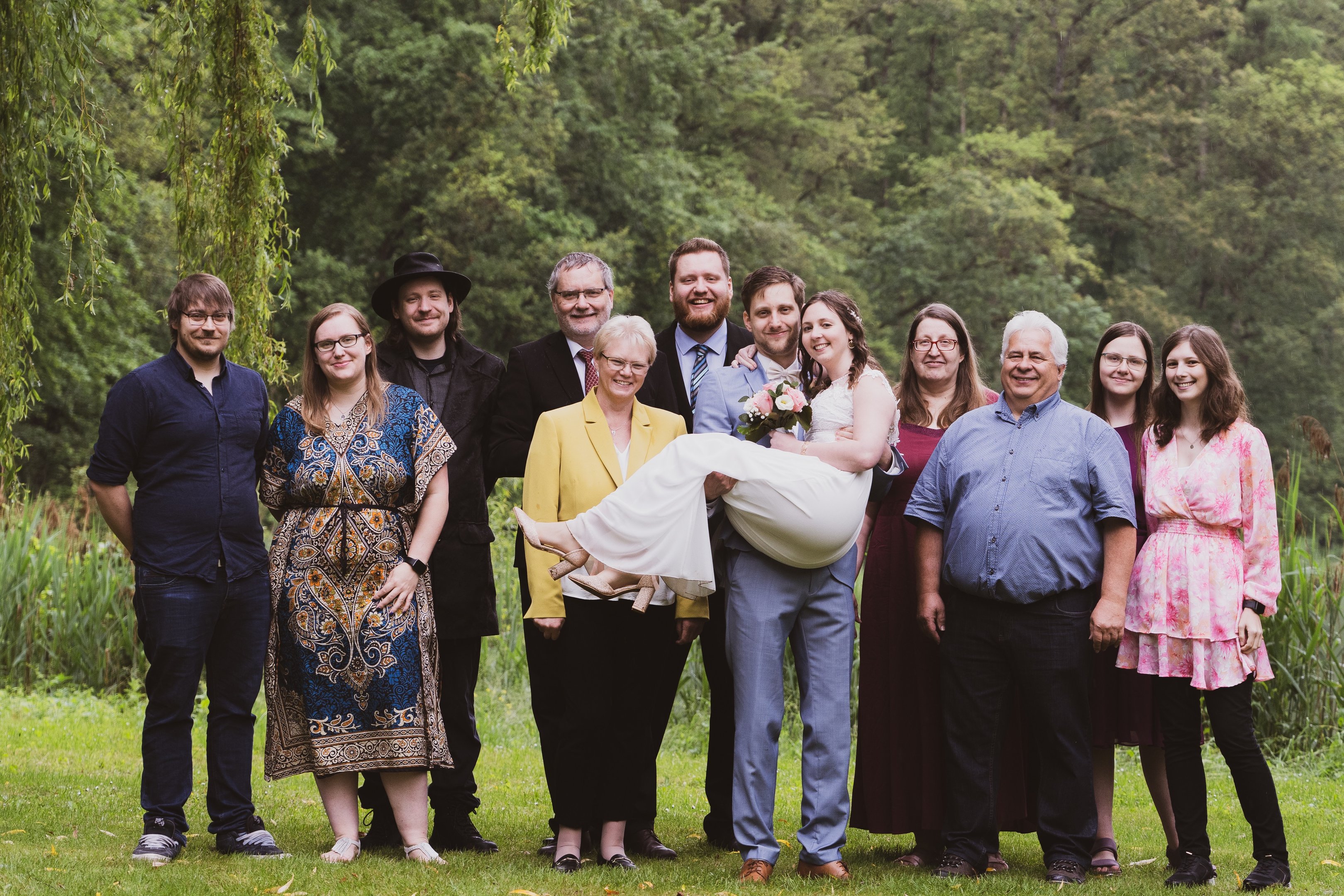 Hochzeitsfoto von Gästen und dem Hochzeitspaar im Grünen, Alle lachend