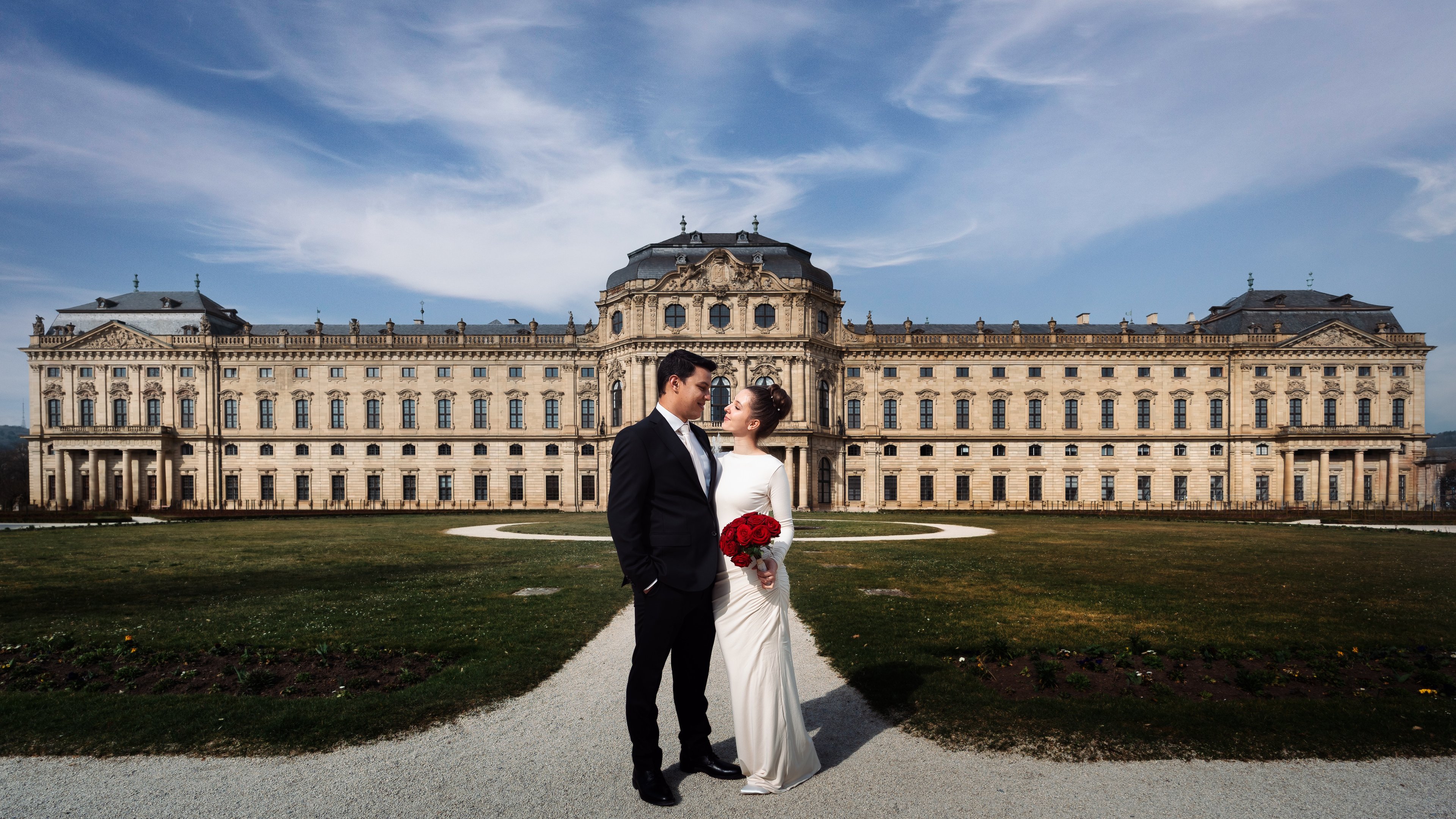 Hochzeitsfoto vom Hochzeitspaar mit rotem Brautstrauß vor einem Schloss in Deutschland