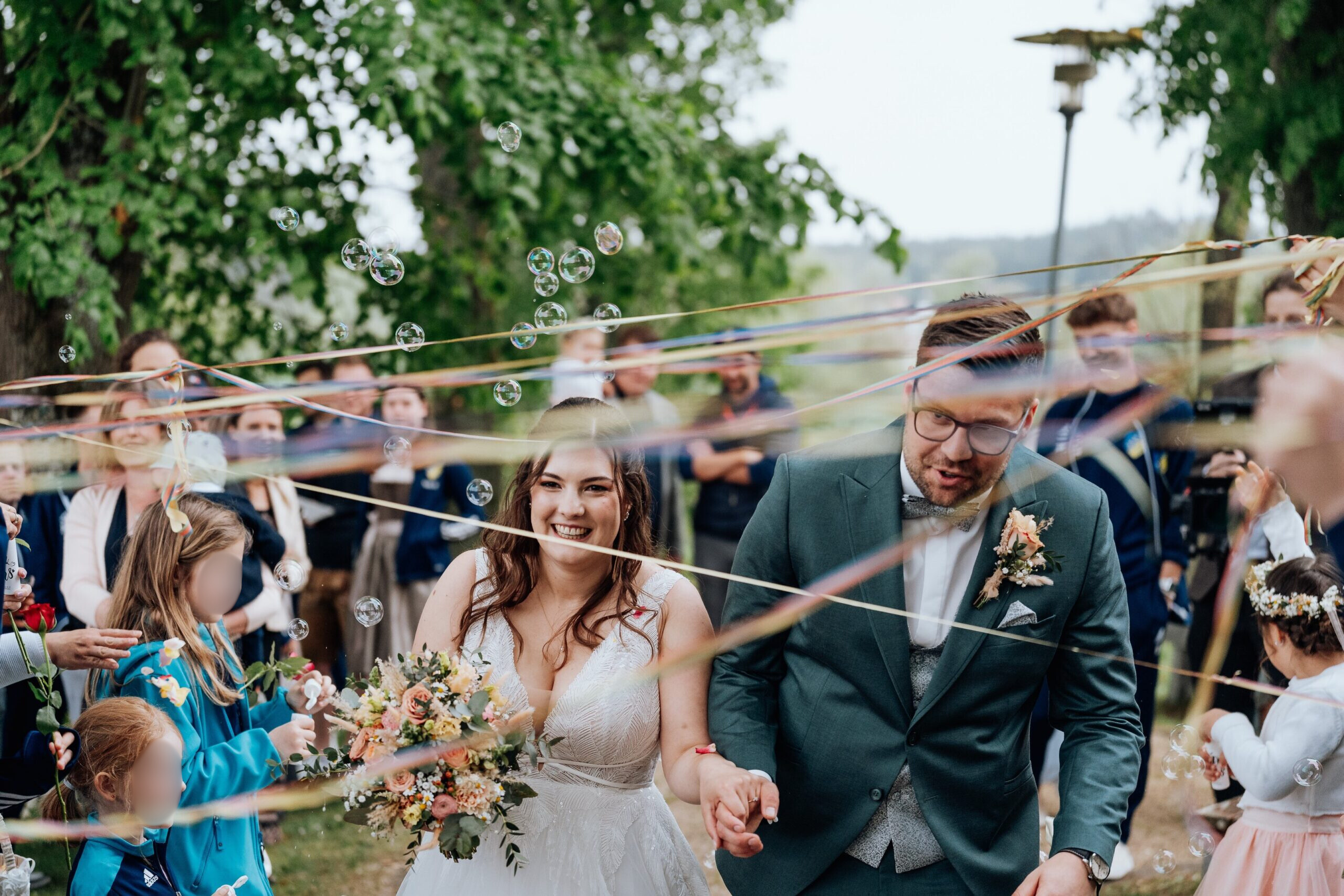 Feierlichkeit und Auszug nach der kirchlichen Trauung - Brautpaar von Gästen umgeben. läuft durch Luftschlangen und Seifenblasen